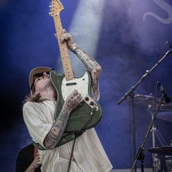 Der fotografierte Gitarrist hält seine Gitarre senkrecht in die Höhe während er darauf spielt. Auch sein Kopf liegt im Nacken, er schaut in die Luft.
