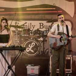Zwei Musiker auf der Bühne, links eine Frau am Keyboar, rechts ein Mann an der Gitarre. Beide haben ein Mikrofon vor sich stehen und singen.