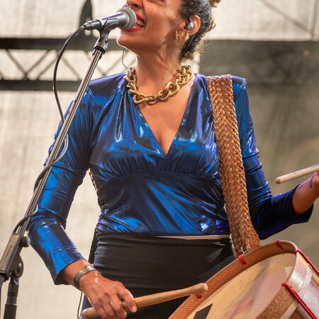 Ayom hat eine Trommel umhängen, auf welcher sie spielt und sind dabei in ein Mikrofon.