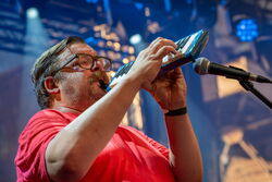 Das Bild zeigt einen Mann im roten Oberteil, welcher auf einer Melodica spielt.