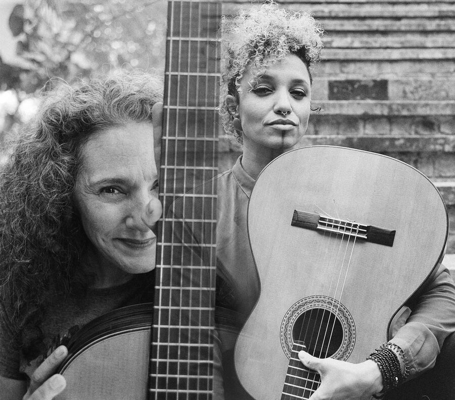 Das schwarz-weiß Bild ist durch den Hals einer Gitarre in zwei Hälften aufgeteilt. Auf der linken Seite sieht man Badi Assad, welche lockige lange Haare hat und ein dunkles Shirt trägt. Sie lächelt freundlich in die Kamera. In ihren Händen sieht man eine