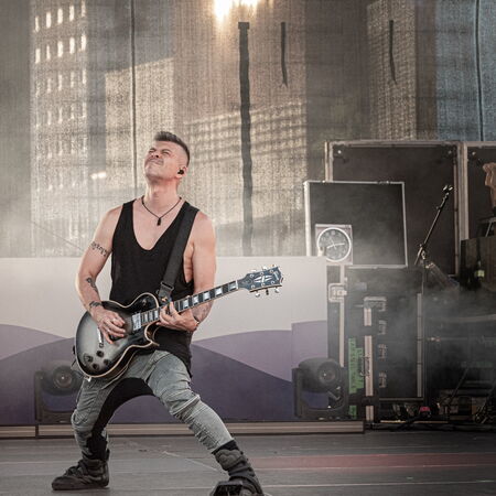 Ein Mann in grauer Hose und schwarzem Oberteil, welcher leidenschaftlich Gitarre spielt.