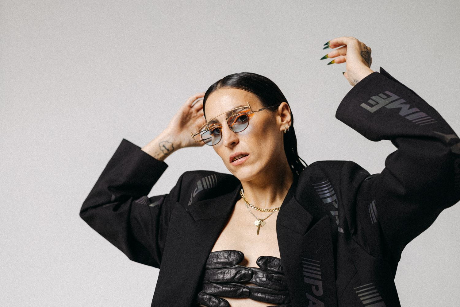 Das Bild zeigt Mine mit einem modernen und selbstbewussten Look. Sie trägt eine auffällige Sonnenbrille, die den Blick akzentuiert. Das schwarze Outfit ist extravagant und trendbewusst, ein maßgeschneiderter Blazer und ein auffälliges Oberteil.