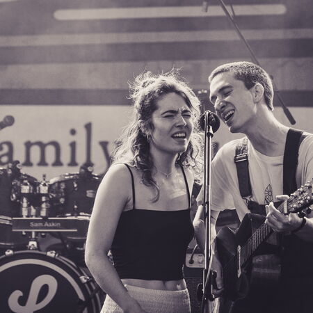 Das Bild zeigt zwei Musiker, die sich ein Mikrofon teilen. Links eine Frau und rechts ein Mann mit Gitarre.
