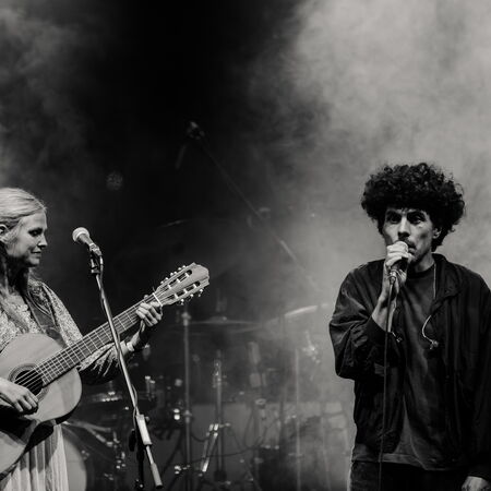 Das schwarz-weiß Bild zeigt links eine Frau mit Gitarre. Rechts einen Mann mit Mikrofon, welcher gerade singt. Die Atmospähre ist durch Nebel sehr mystisch.