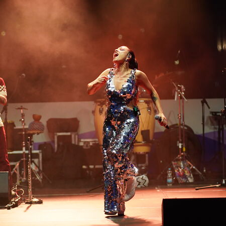 Das Bild zeigt eine Sängerin im Glitzer-Outfit, welche ausgelassen Tanzt. Im Hintergrund ein Mann der Saxophon spielt.