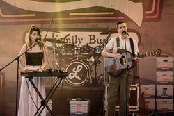 Zwei Musiker auf der Bühne, links eine Frau am Keyboar, rechts ein Mann an der Gitarre. Beide haben ein Mikrofon vor sich stehen und singen.