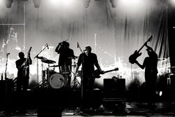 Schwarz-weiß Foto einer vierköpfigen Band von welcher durch die Belichtung nur die Silhouetten erkennbar sind.