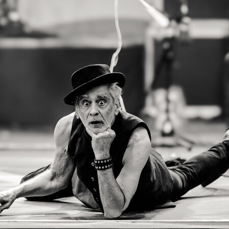 Das schwarz-weiß Bild zeigt Melingo, wie er auf dem Bauch liegt und seinen Kopf auf dem linken arm abstützt. Seine Augen sind weit aufgerissen und er trägt einen Hut.